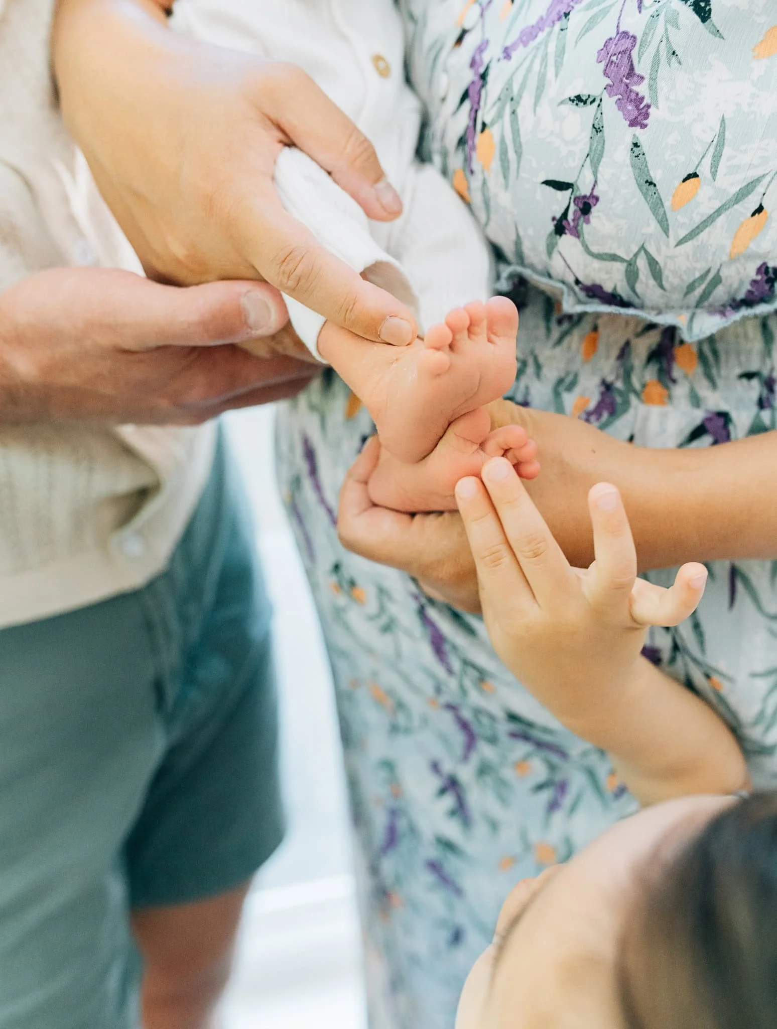 Close-up of baby foot with mom and dad holding it and baby brother reaching for it
