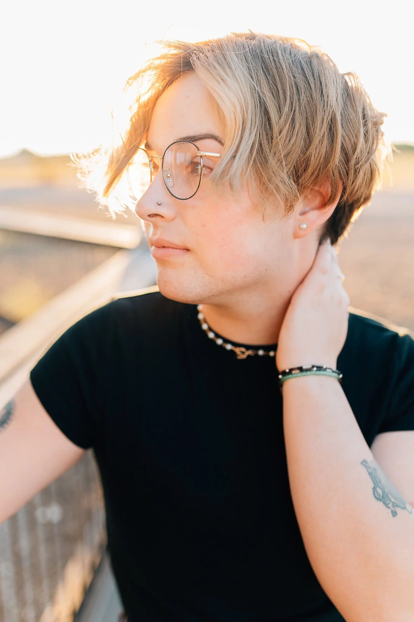 Senior boy in black shirt and glasses with hand on neck and looking away
