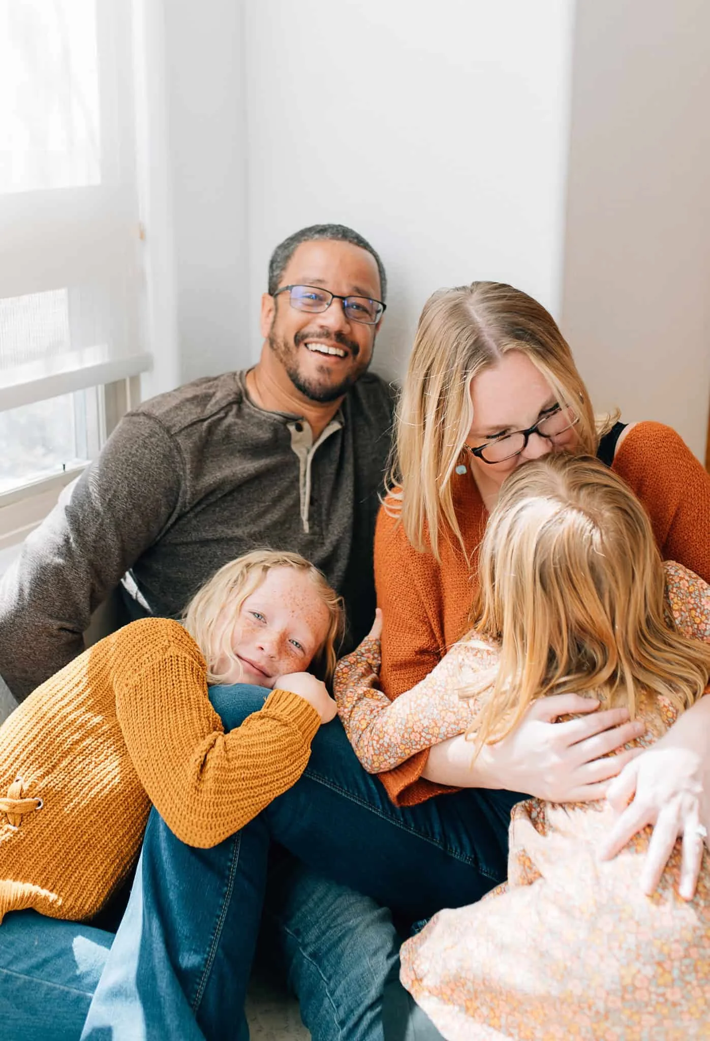 mom and dad sitting with two girls piling on top of them
