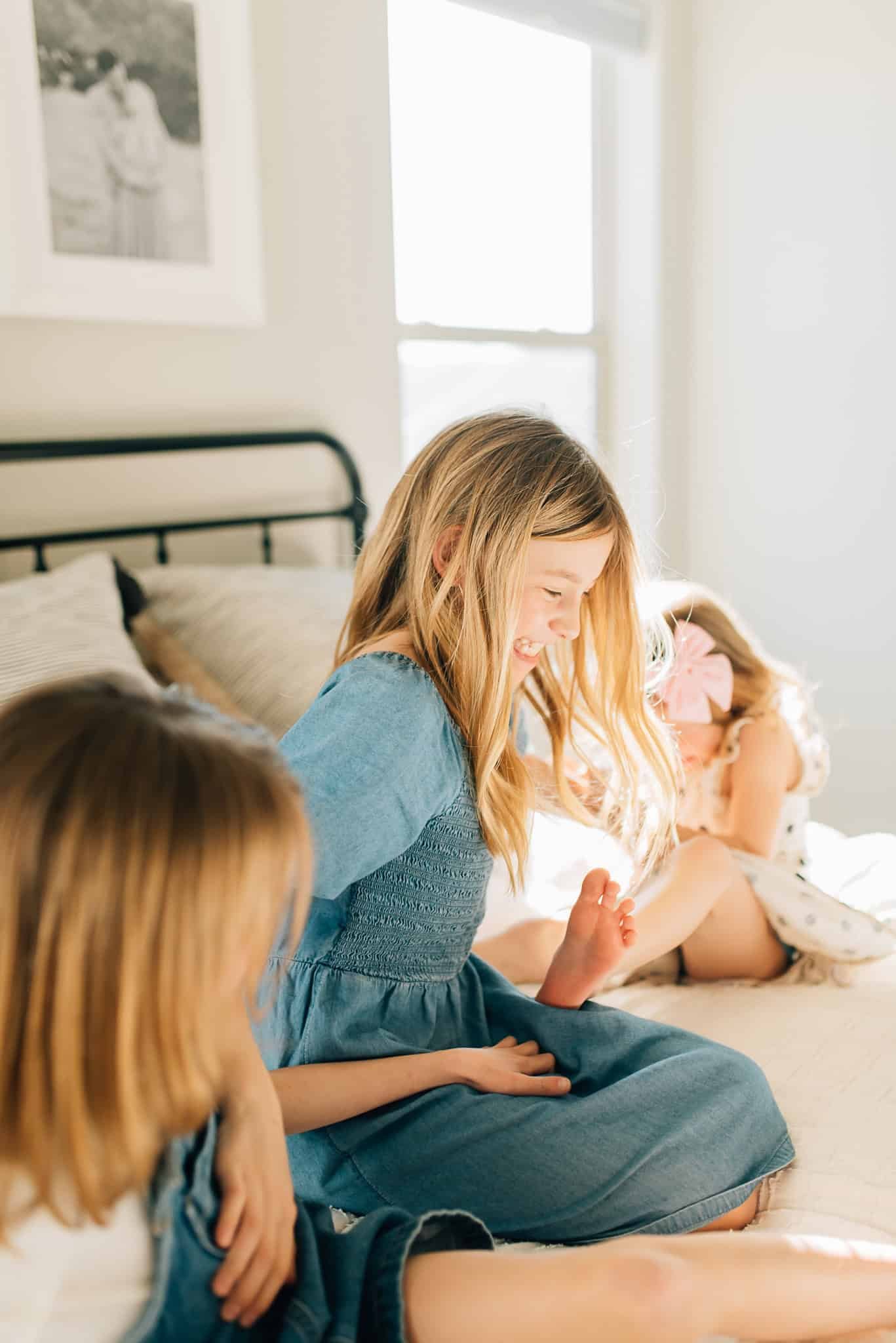 three sisters sit on a bed and tickle each other