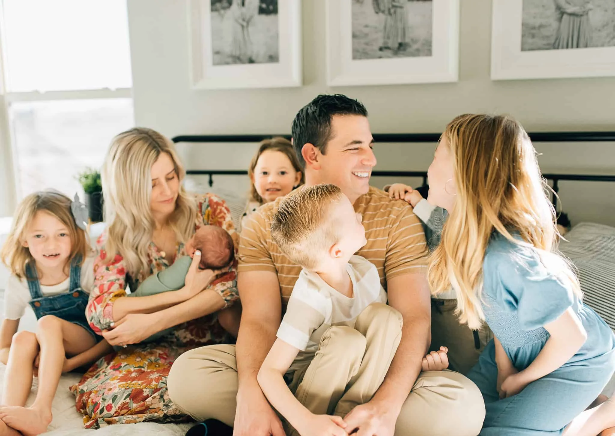 Family with six kids sits on bed and laugh together, mom holds newborn baby