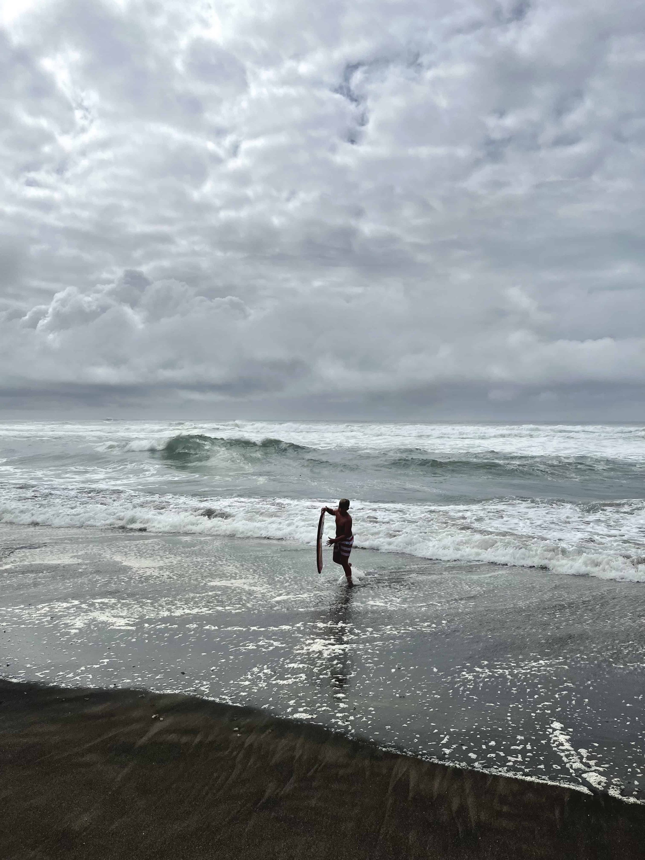 Dark silhouette of boy carrying a boogie board out of the water to the shore at Neskowin Beach