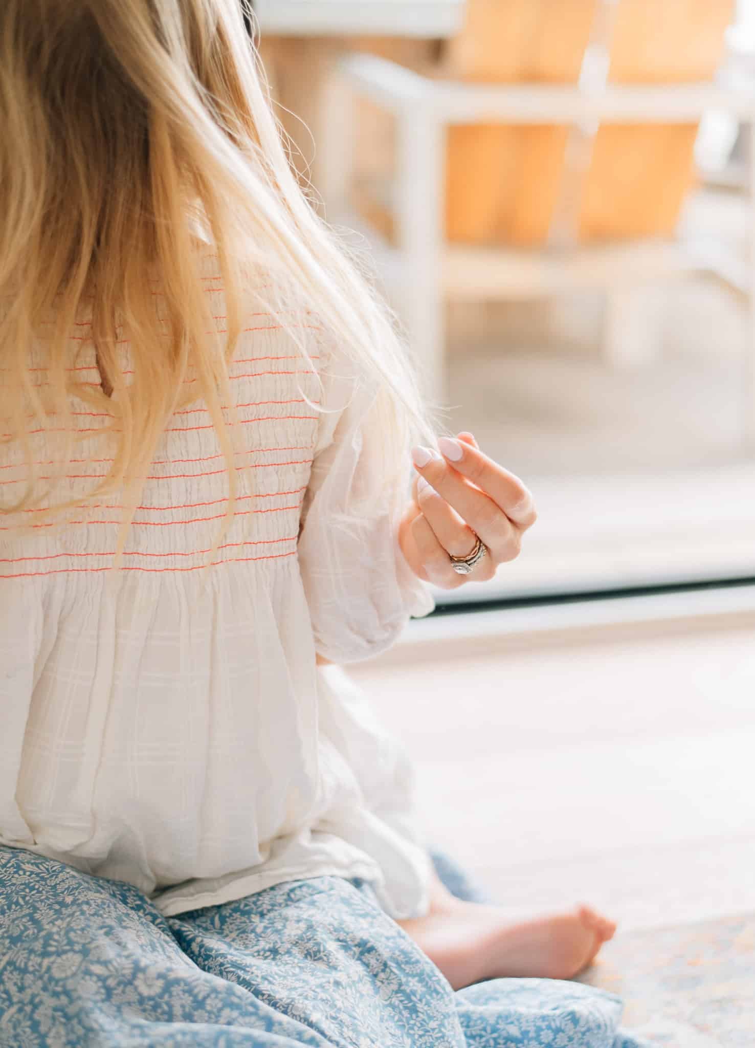 detail of mom's fingers playing with daughter's blonde hair while she sits on her lap