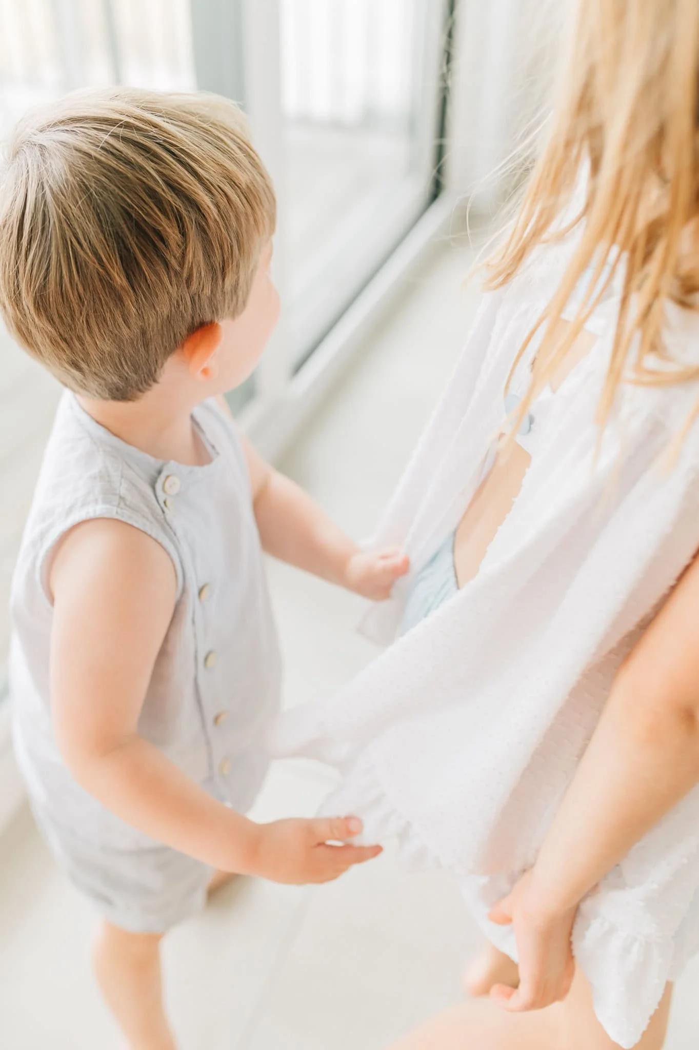 baby brother reaches for sister's dress as she runs away