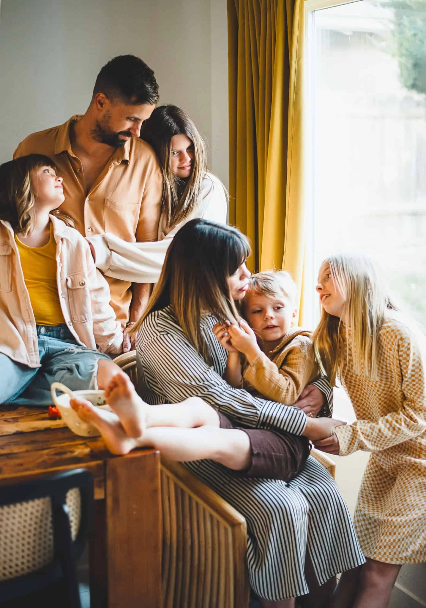 Mom sitting in chair by dining room table while her husband and kids surround