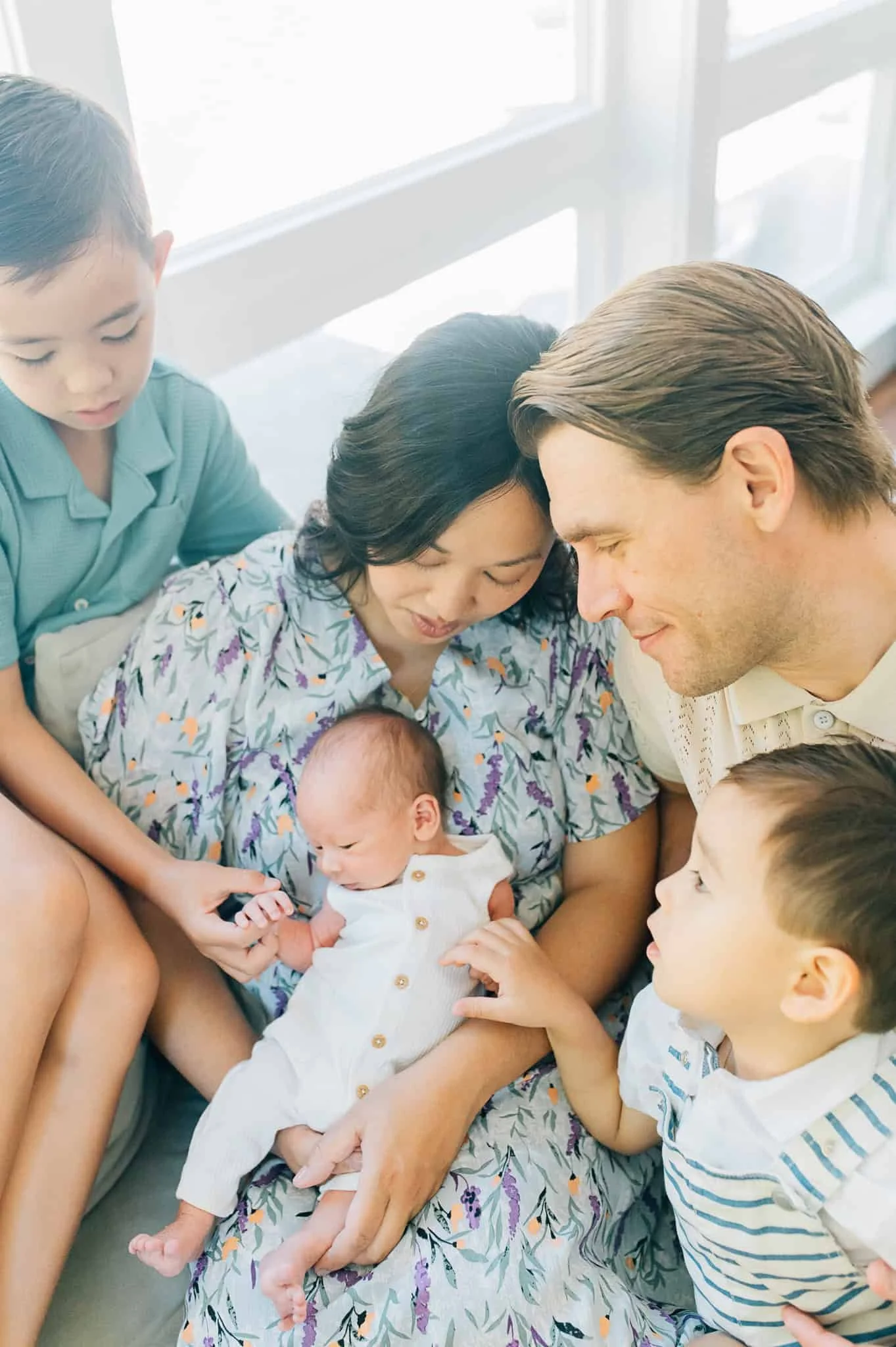 mom holds newborn baby on lap while two sons and dad snuggle her