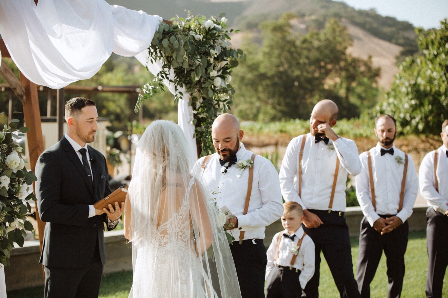 groom reads vows to his bride as his groomsmen look on at his higuera ranch wedding. ca wedding photographer