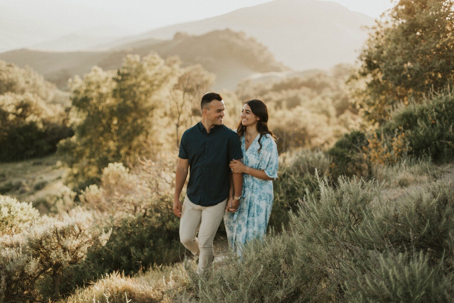 couple walks hand in hand through the lush green hills of paso robles as the sun sets during their engagement photoshoot. paso robles wedding photographer poppy &amp; vine