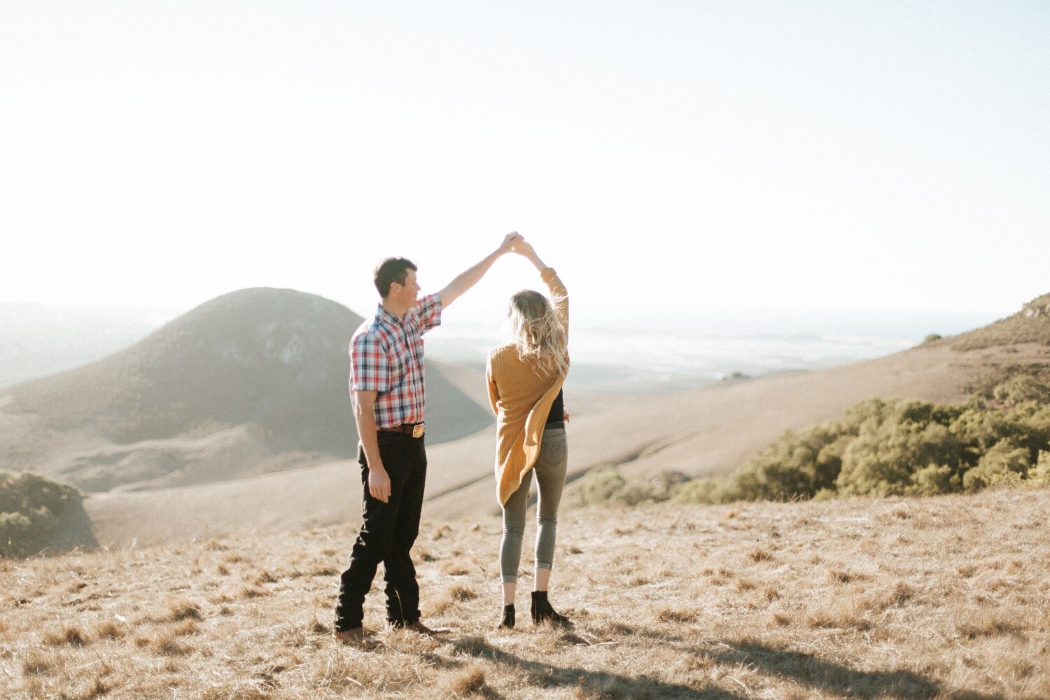 man twirls woman as the sun sets behind them during their morro bay engagement photo session, captured by san luis obispo engagement photographer poppy and vine