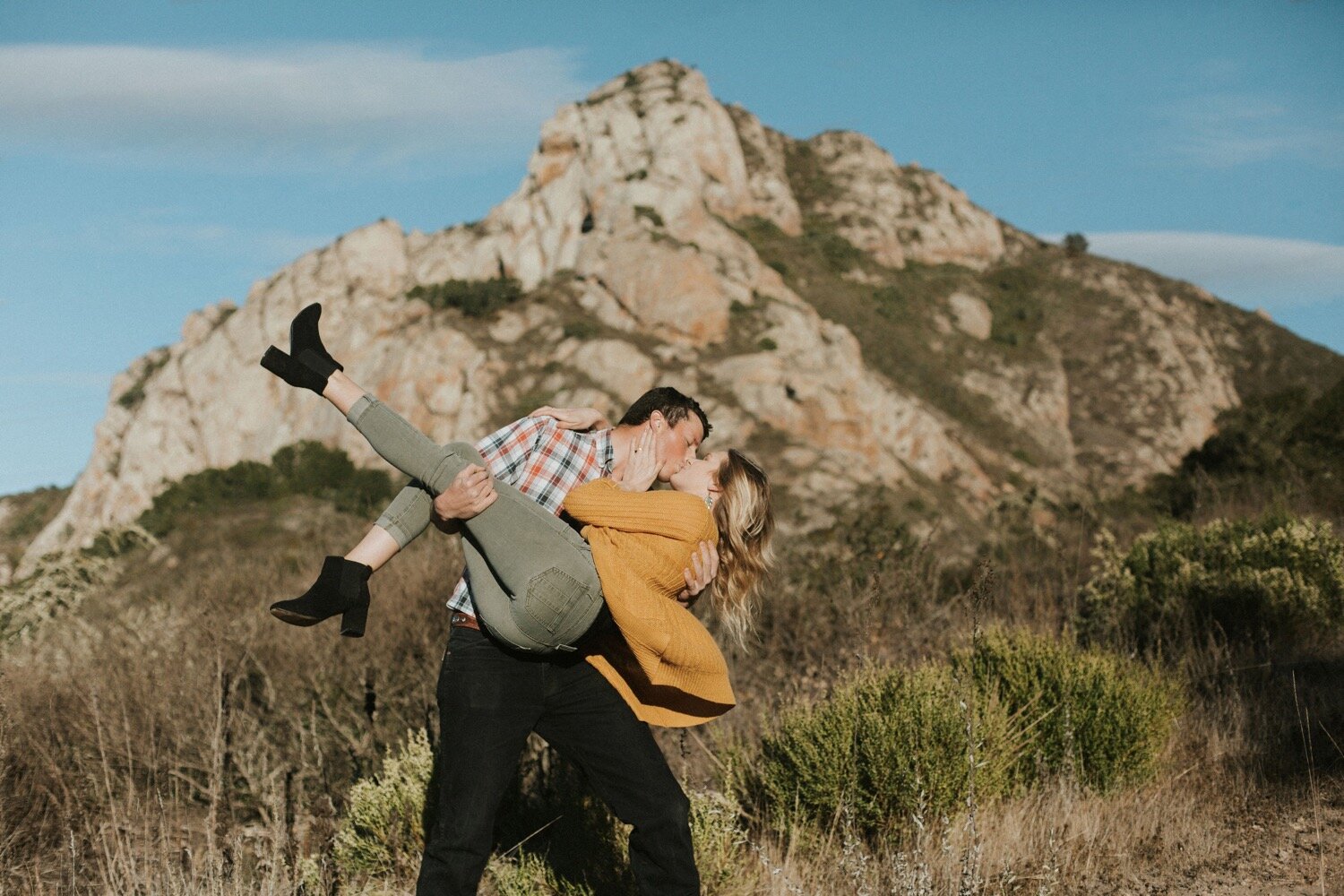 man dips woman in front of hollister peak in san luis obispo, during their morro bay engagement photoshoot, captured by san luis obispo photographer poppy and vine