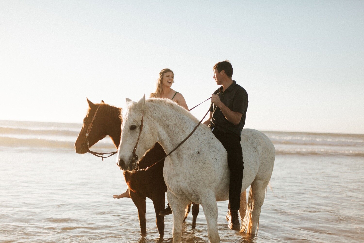 couple rides horses in the ocean at morro bay beach, captured by slo wedding photographer poppy and vine