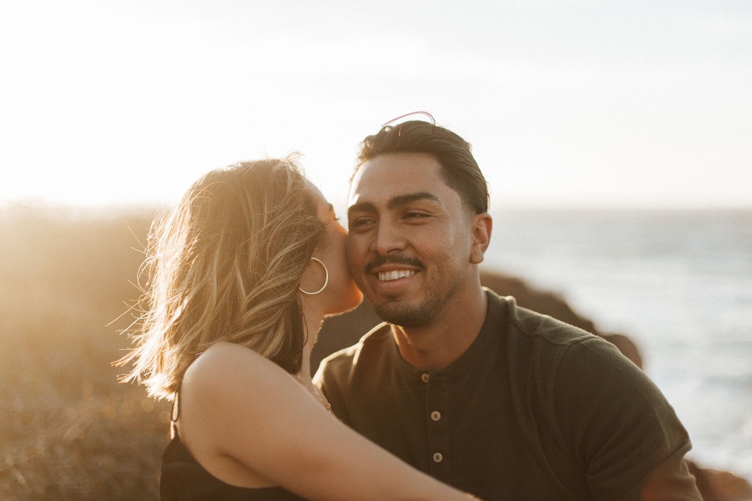  woman kisses man’s cheek during their golden hour couple photoshoot on the bluff trail at montana de oro state park in california, captured by san luis obispo wedding photography duo poppy and vine 