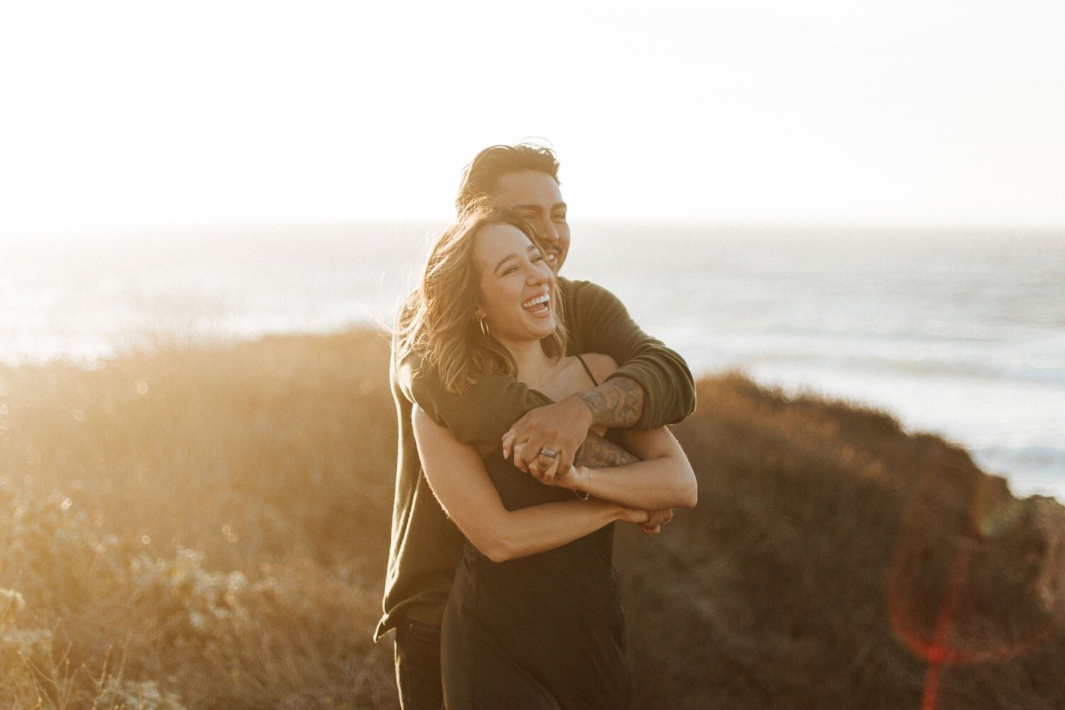  couple holds each other and laughs during their sunset couple photoshoot on the bluff trail at montana de oro state park in los osos, california, captured by slo wedding photographer poppy and vine 