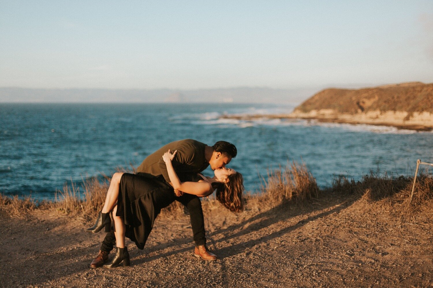  man dips woman and kisses her during a couple photoshoot on the bluff trail at montana de oro state park in los osos, california, captured by san luis obispo wedding photographer poppy and vine 