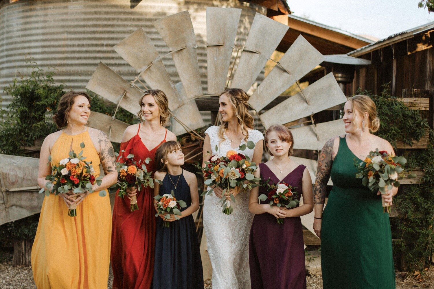  bride and her bridesmaids, wearing different jewel toned bridesmaid dresses, hang out on the rustic property at dana powers house in nipomo california. this rustic fall wedding was captured by san luis obispo wedding photographers poppy and vine 