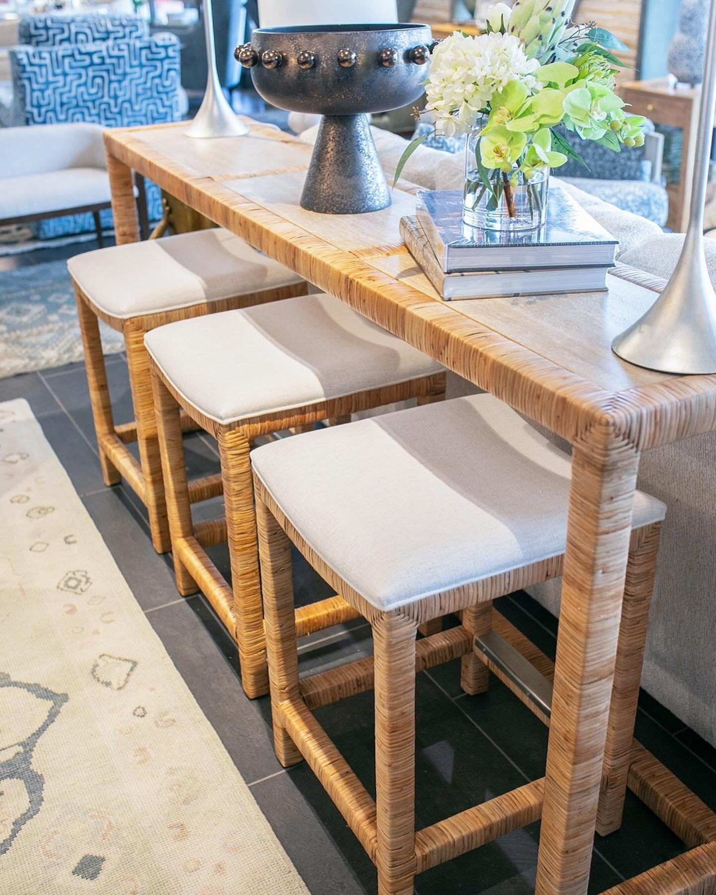 Bring a bit of the beach to your home with this rattan console featuring inset honed Becagli stones and three ivory upholstered stools. #CoastalVibes #ExtraSeatingForSummer #HenryHomeInteriors