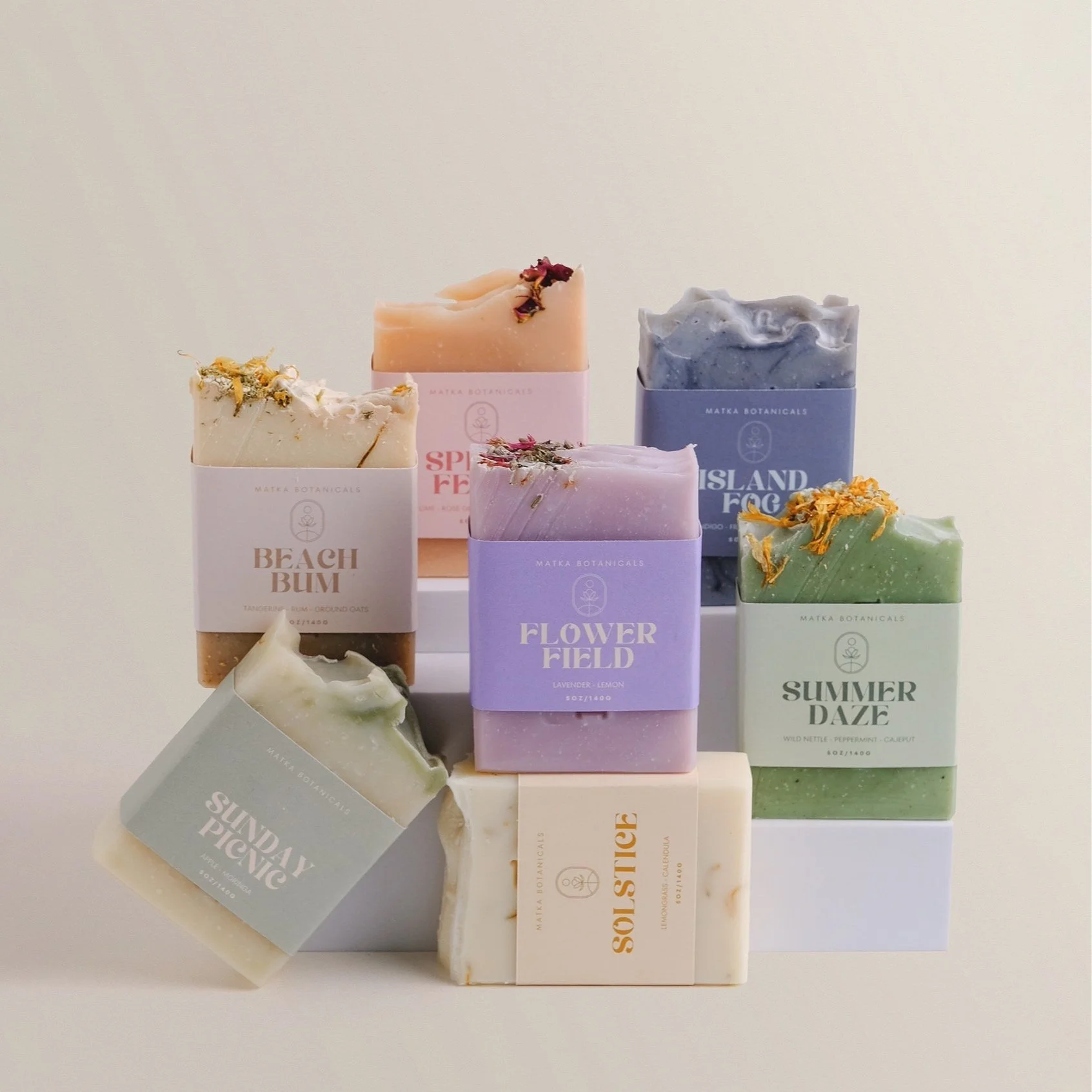 Collection of colorful soap bars, each with labels and decorative toppings, arranged on a white display stand.