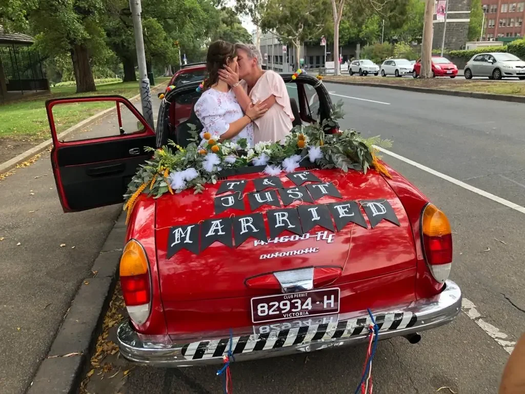 Same sex couple celebrating with a just married sign in their car after eloping in Melbourne with I Do Drive Thru