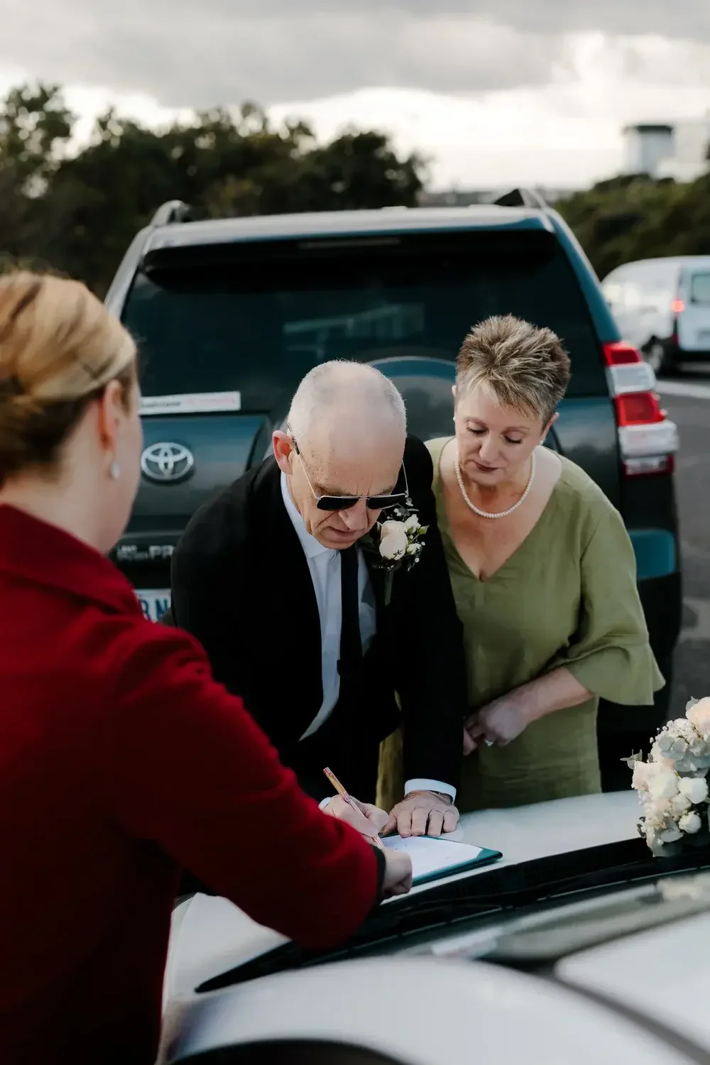 Couple signing their marriage paperwork on the bonnet of a car with I Do Drive Thru — legals only ceremony from $400