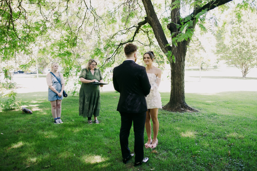 Budget wedding couple smiling outdoors with celebrant and photographer