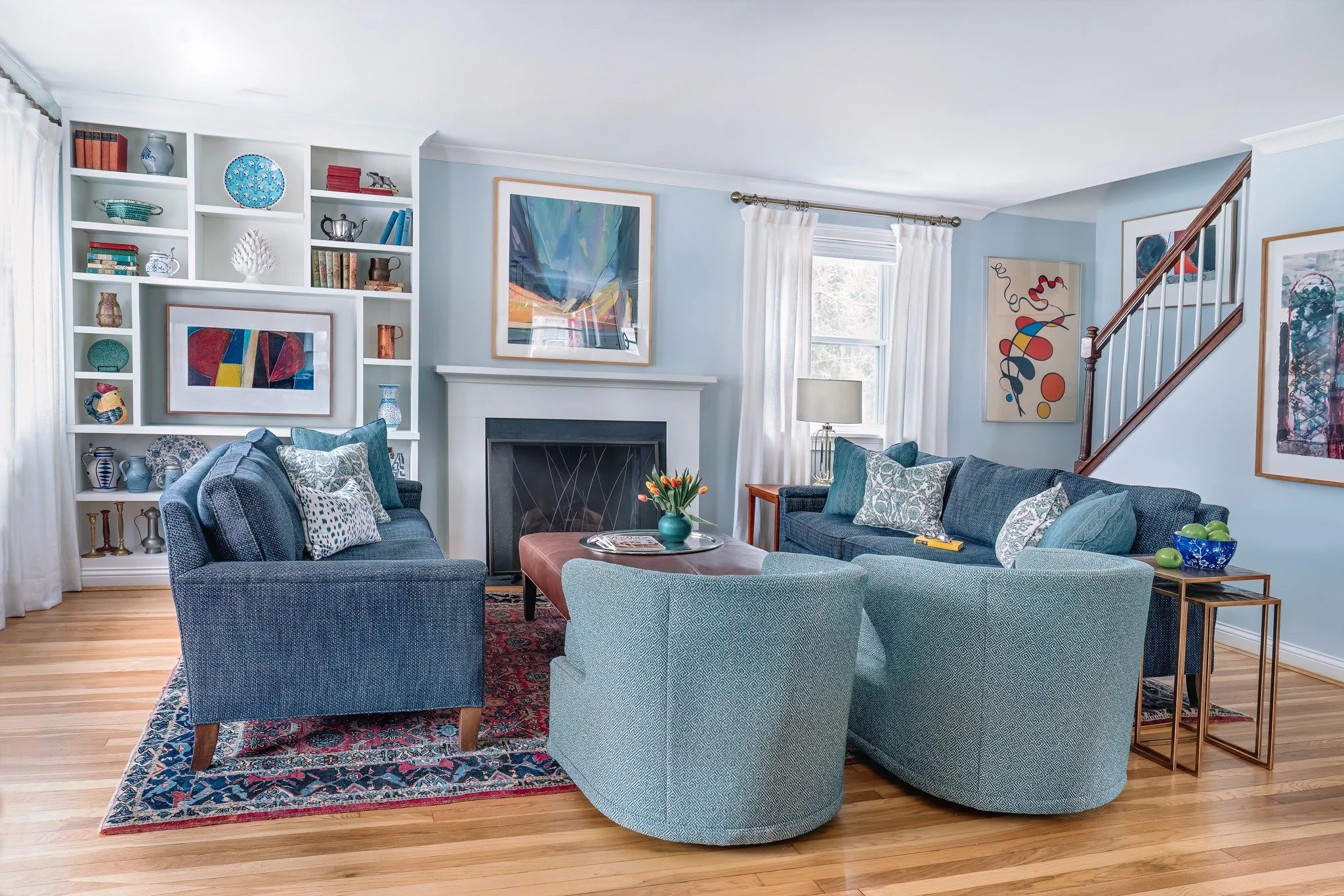 In this space, the art truly drives the design. The bold reds and yellows in the abstract paintings reappear subtly in the rug and in the accessories tucked into the built-ins, while the layered blues from the artwork flow seamlessly into the sofas a