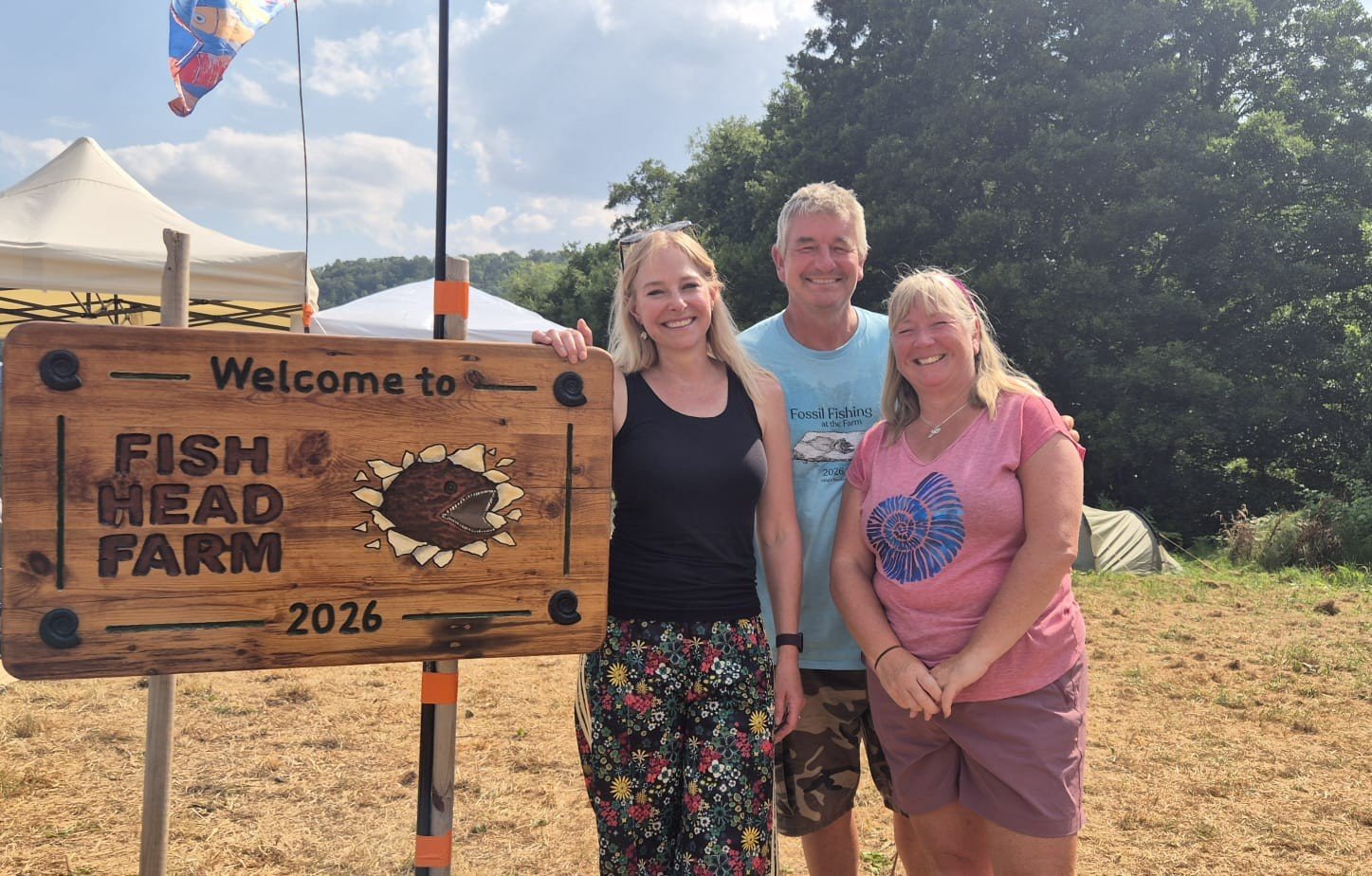 Three people stood next to a sign which reads Fish Head Farm