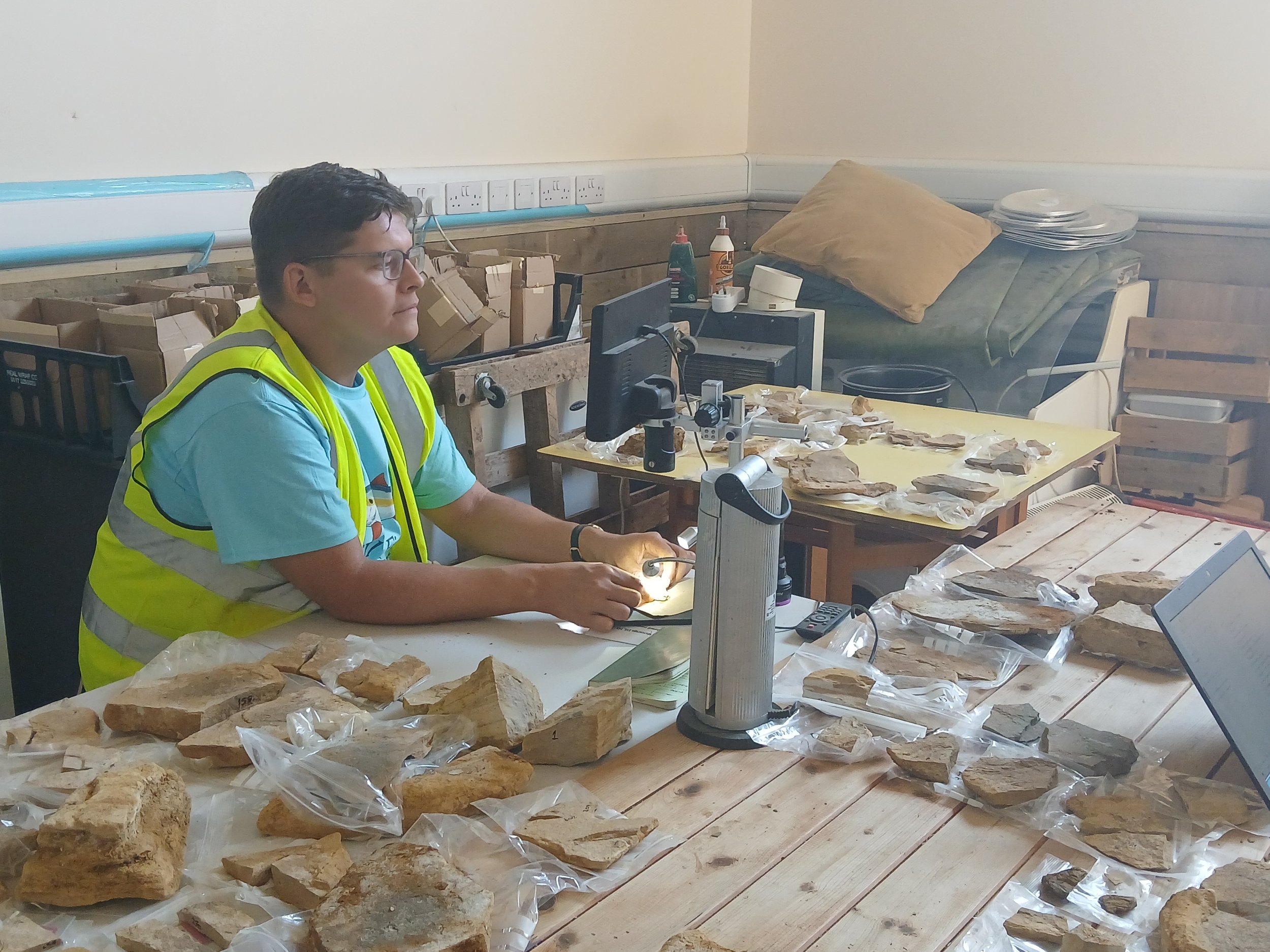 Man sits at a table looking at fossils under a microscope