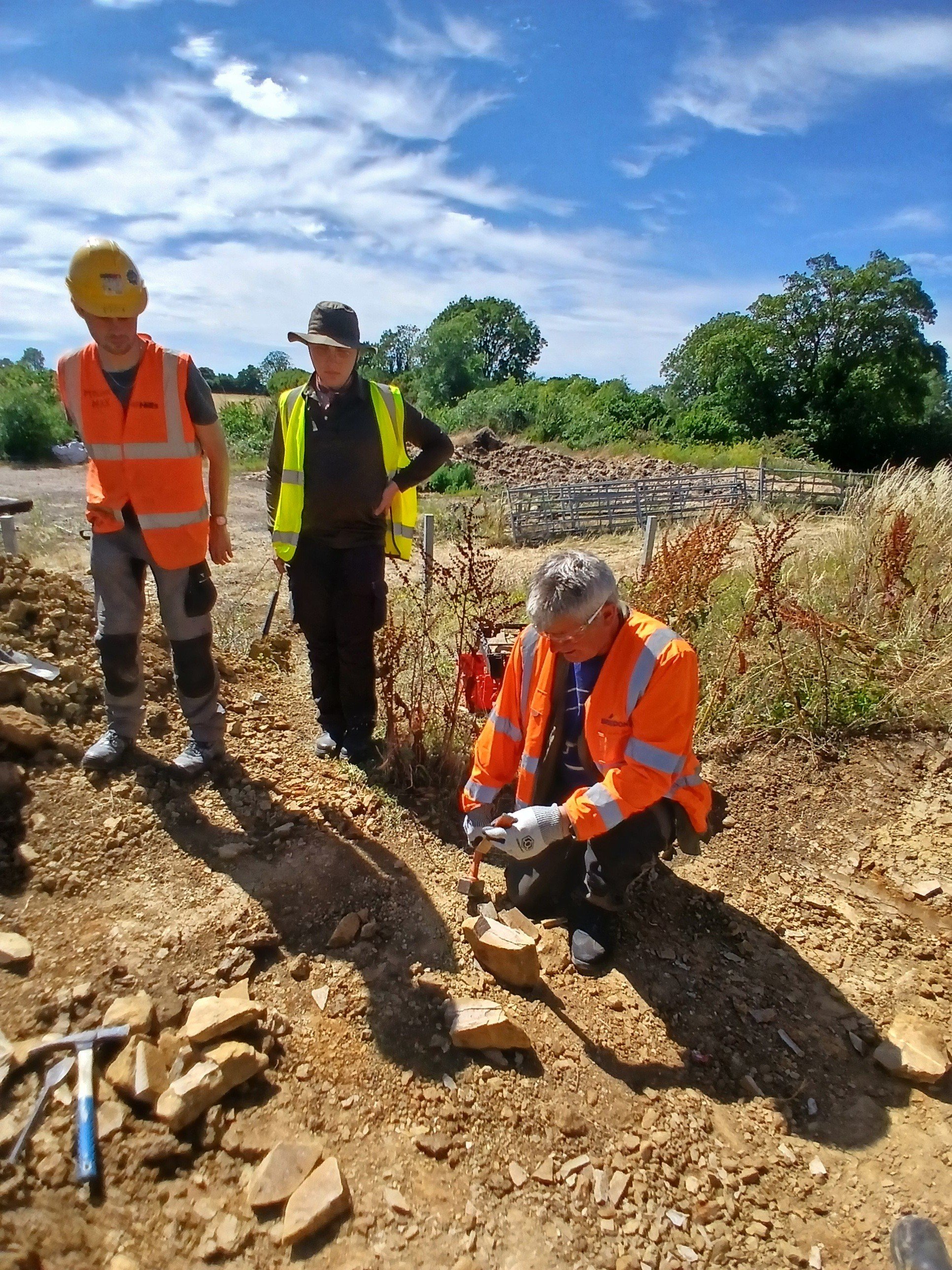 A man in a high vis jacket crouching down chiselling a rock