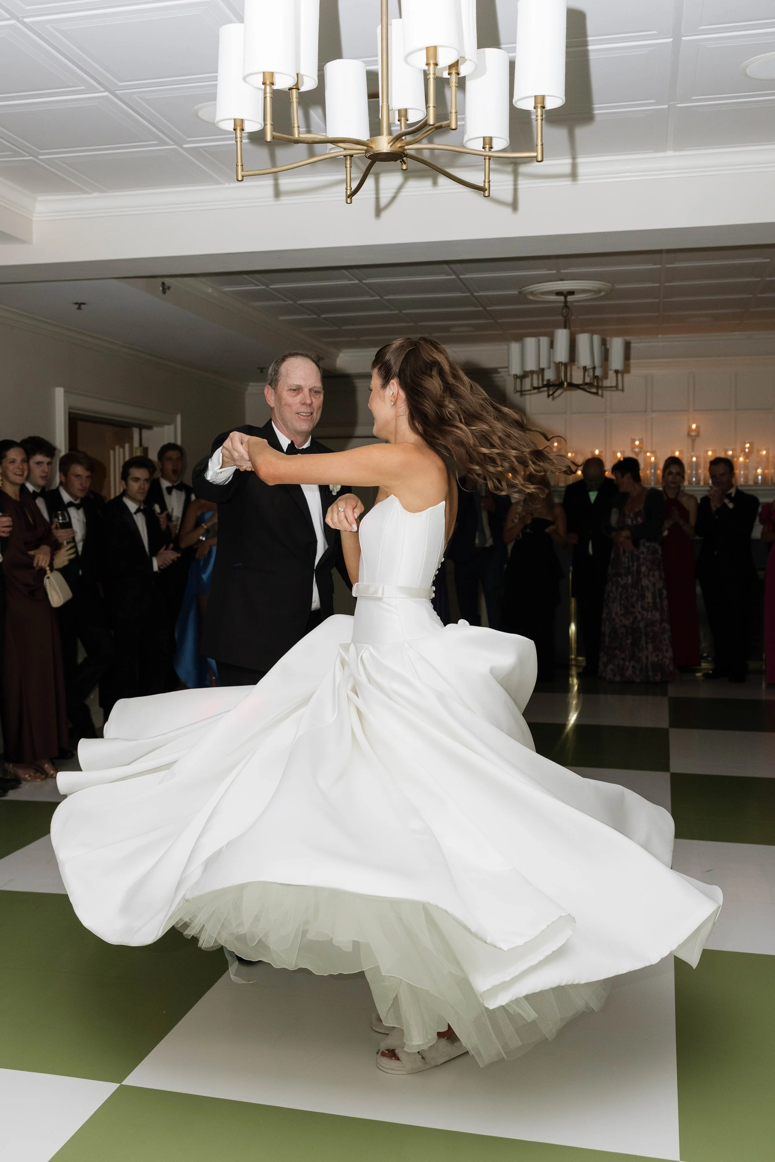 A bride and an older man dancing at a wedding reception, with guests watching in the background.