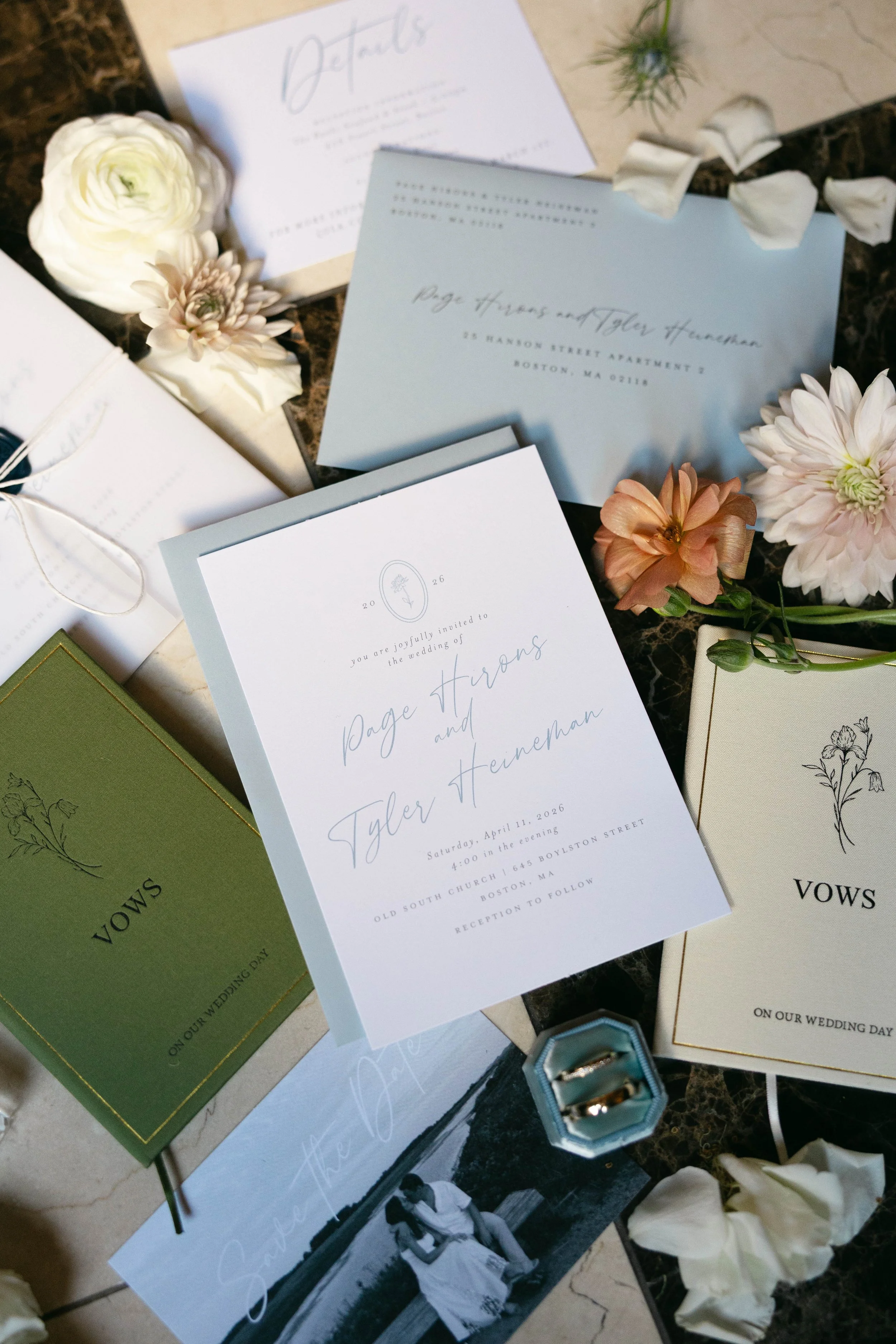 Wedding invitations and cards decorated with flowers and petals on a marble surface.