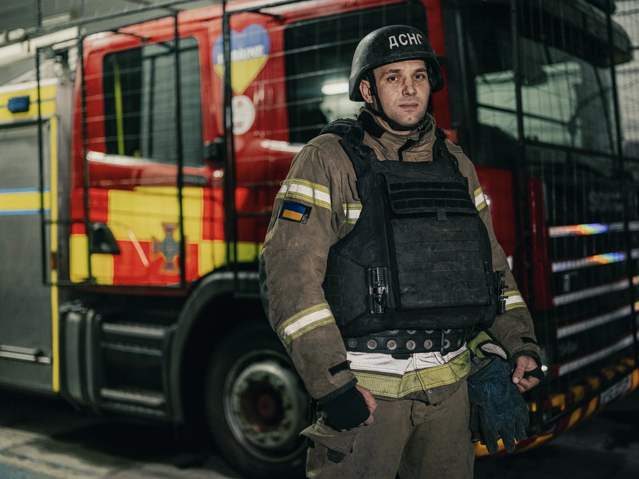 A firefighter in uniform and helmet standing in front of a fire truck.