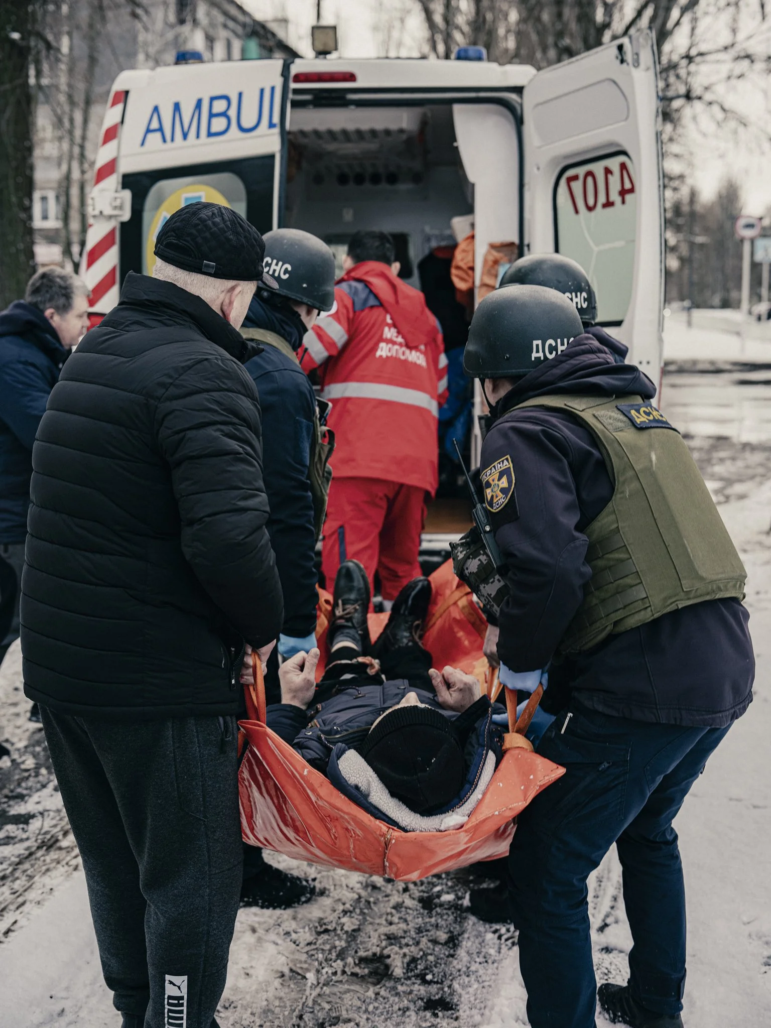 Emergency personnel transfer a patient on a stretcher into an ambulance on a snowy street.