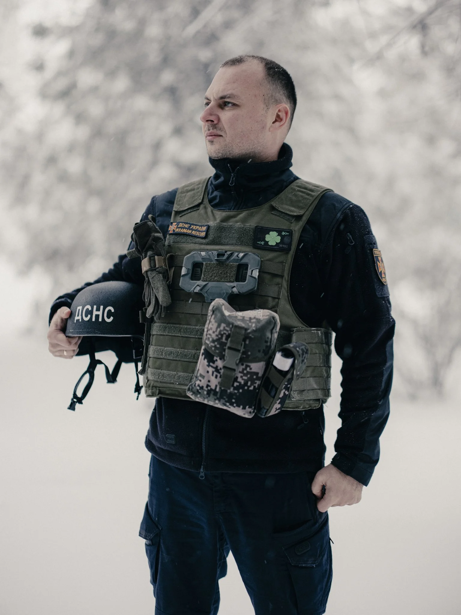 A man in tactical gear outdoors in snowy conditions, holding a helmet with Cyrillic text.