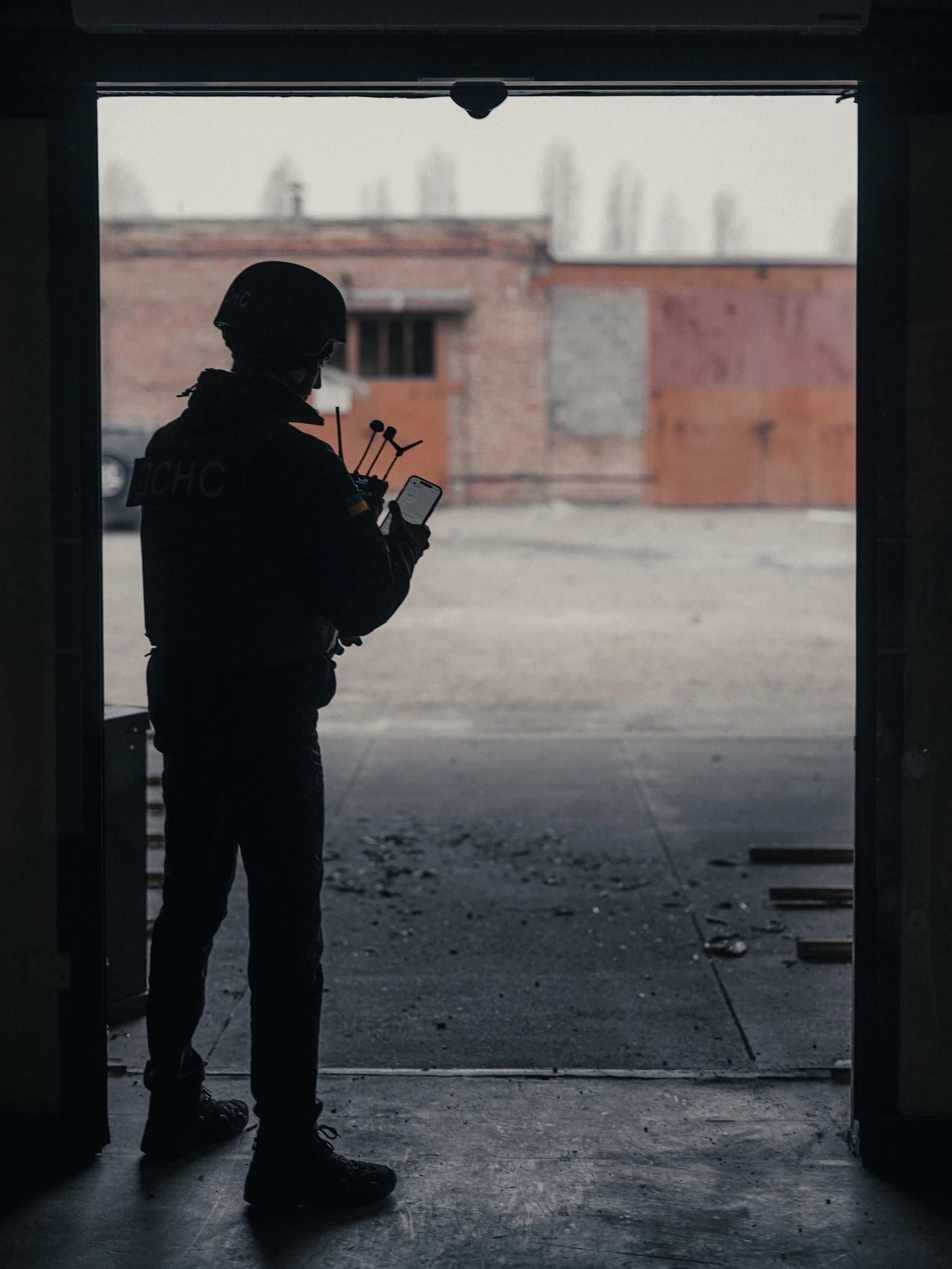Silhouette of a person in tactical gear standing in a garage and looking at a smartphone, with a background of an urban street scene.