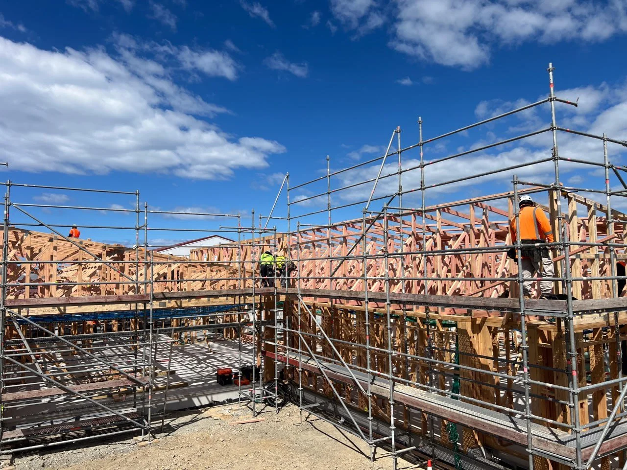 A construction worker wearing a blue helmet and safety gear is on scaffolding at a building site.