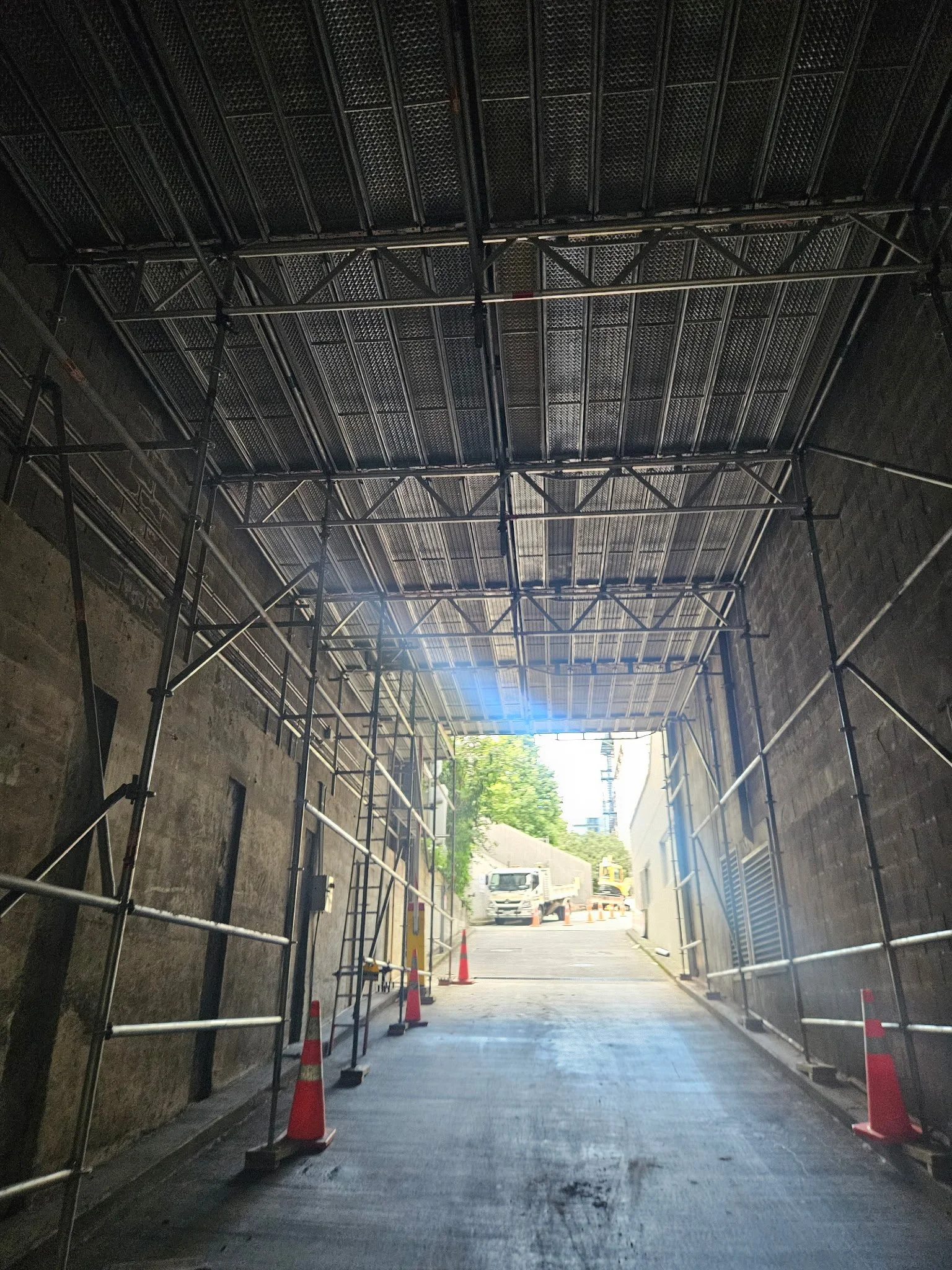 Construction scaffolding and orange traffic cones set up inside a tunnel leading to an outdoor street with vehicles.