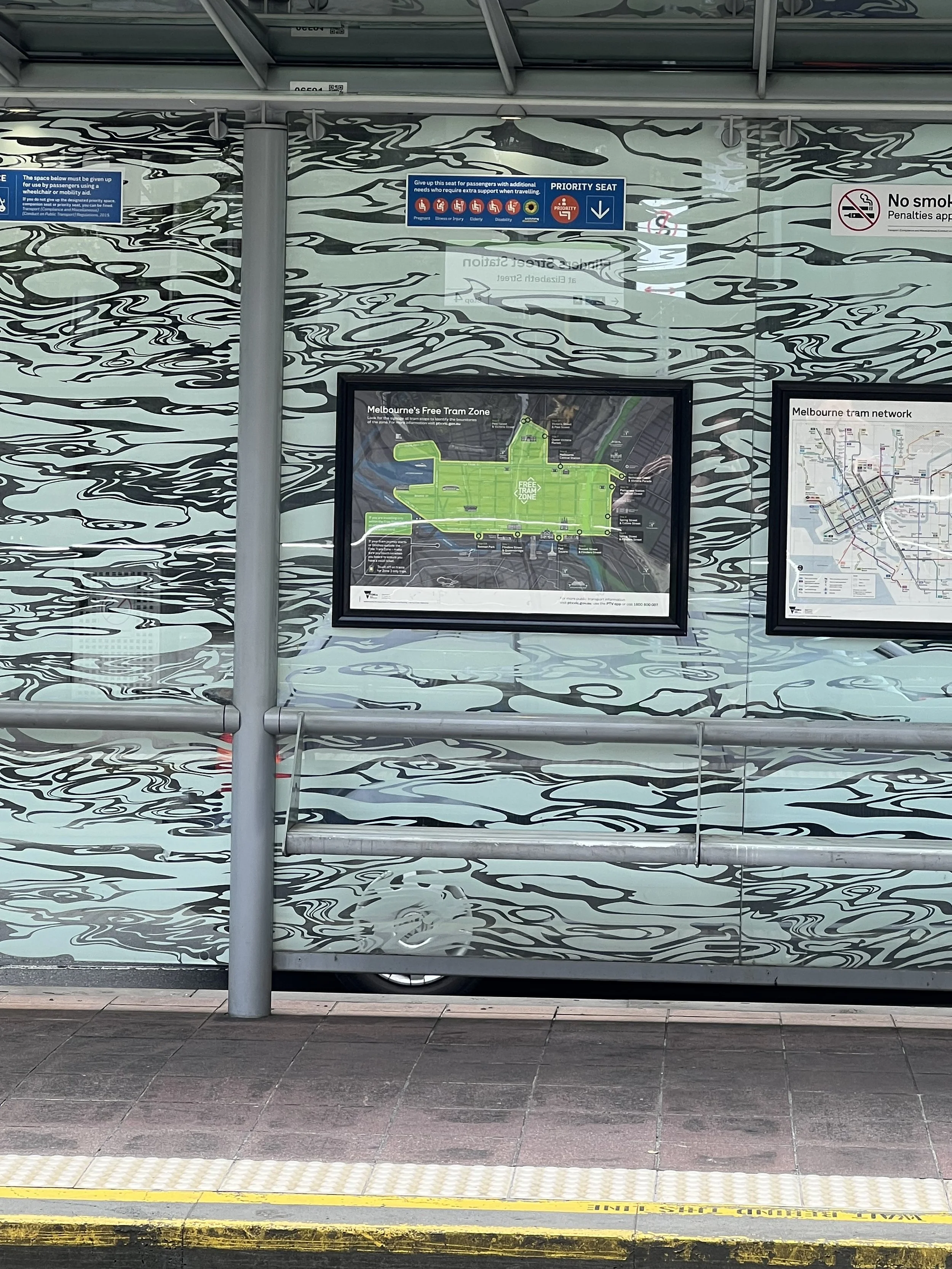  a photo of a raised tram stop platform with two signs. One sign indicates a priority space for wheelchair users and the other is a priority seat sign with pictures indicating the different types of people who may need the seat. The hidden disability