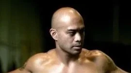 Close-up of a muscular man with a shaved head looking to the side in a dark setting