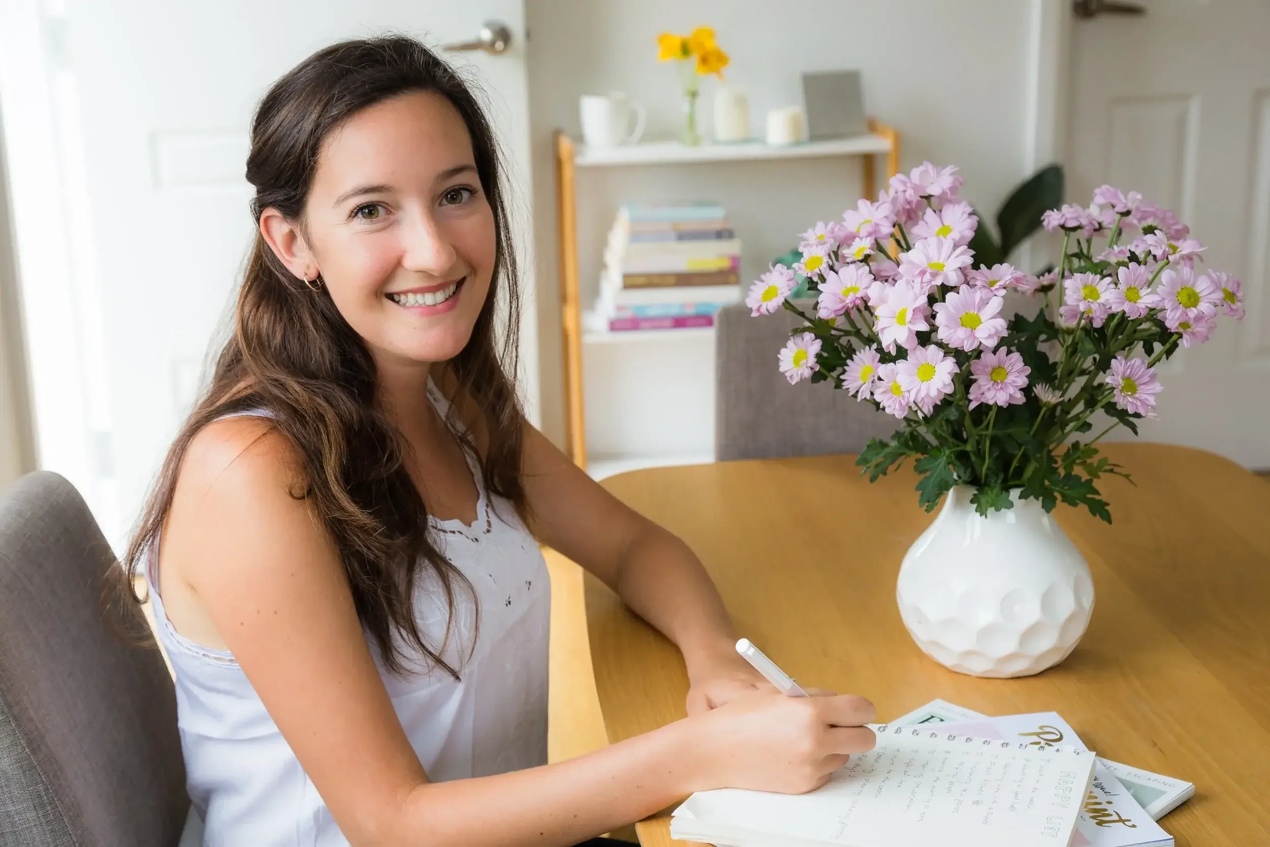 Grace, owner of She Embodies, sitting at the desk writing in a journal, smiling.