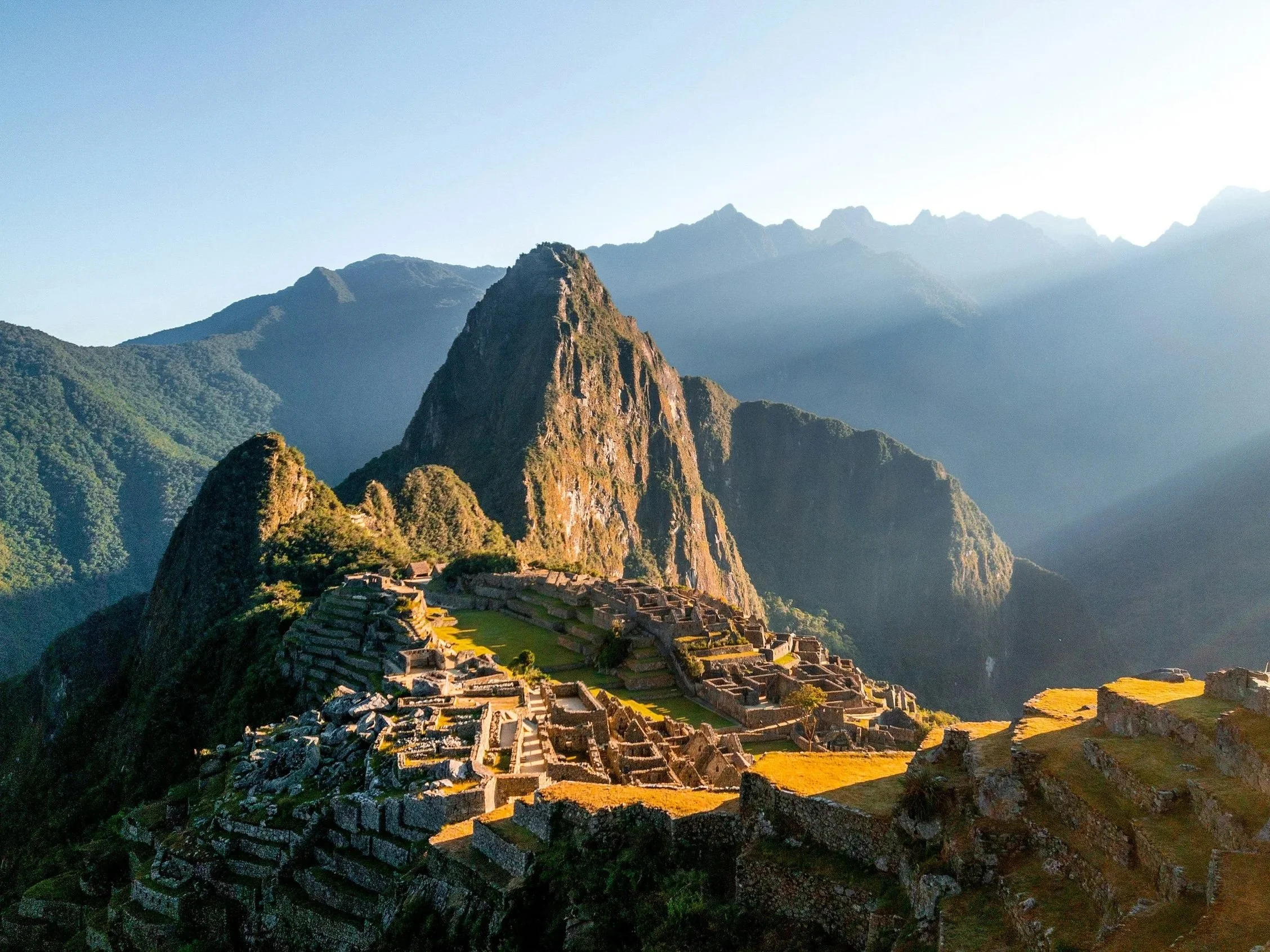 Ancient Incan city of Machu Picchu with ruins set against lush green mountains and a clear sky.