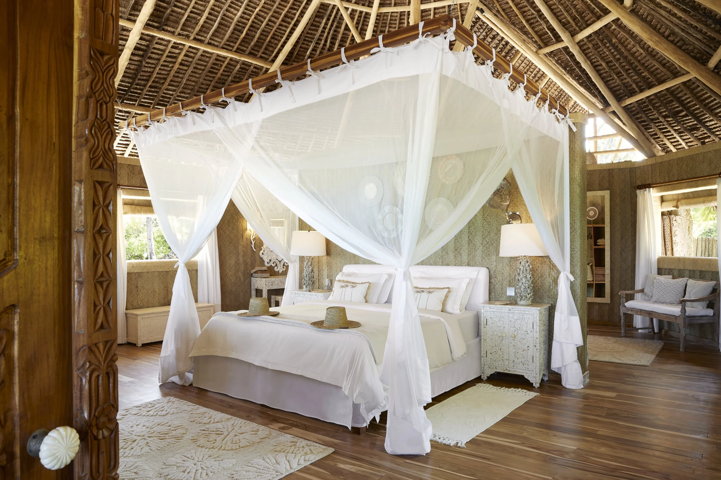 A bedroom with a four-poster bed and white mosquito netting, wooden furniture, and tropical decor.