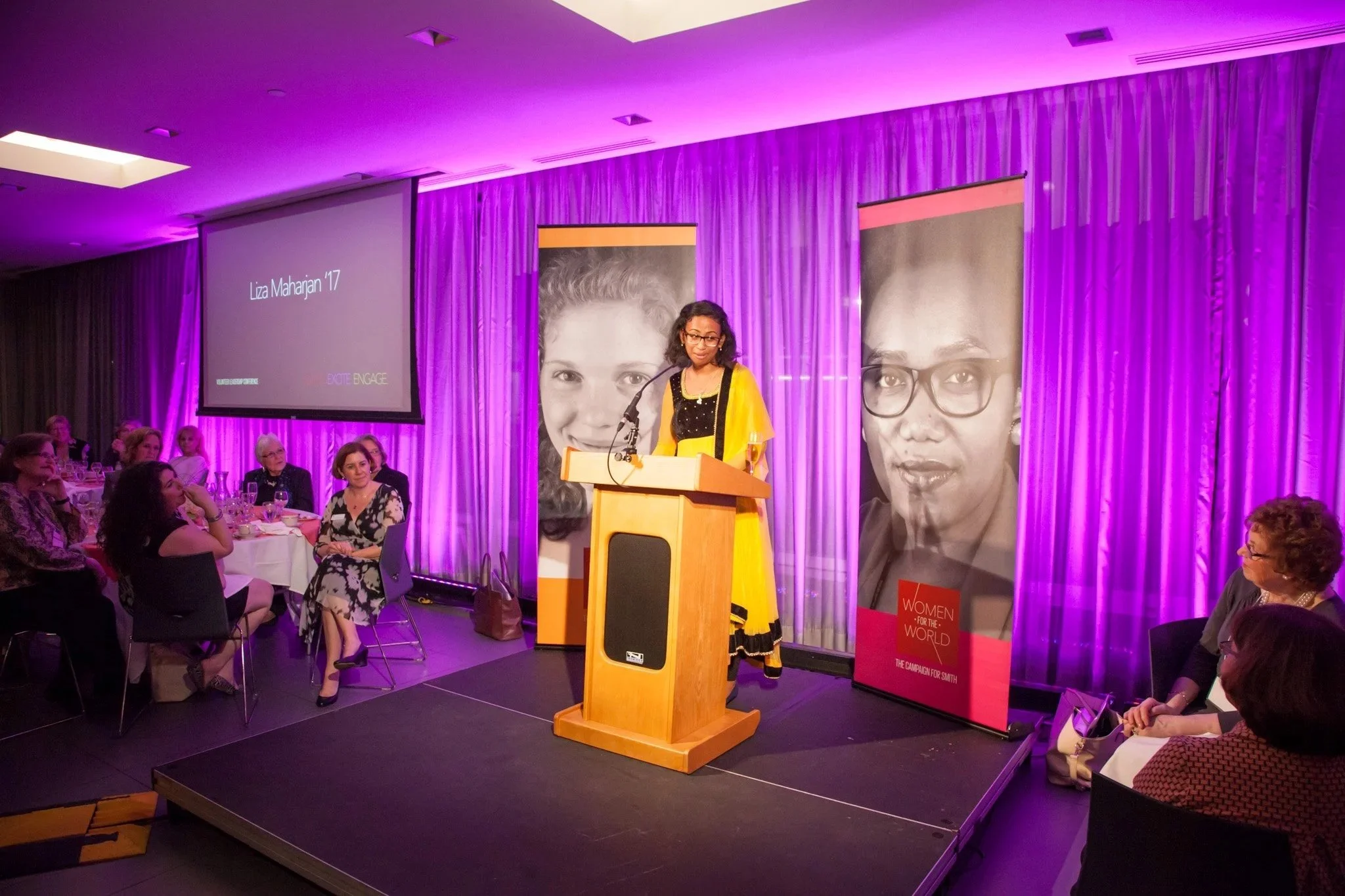  Young woman in a. yellow sari speaks to a crowd at an NYC Corporate event and New York Corporate photographer Elizabeth Solaka is working the event 
