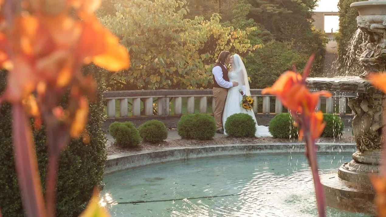 A wedding couple kisses by a fountain