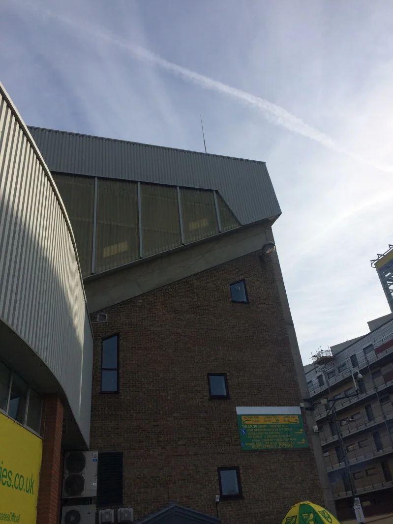The conjunction of the River End and main stand (left) accidentally offers a rare moment of architectural interest. In the background, the Wensum-backing Rotterdammish flats.