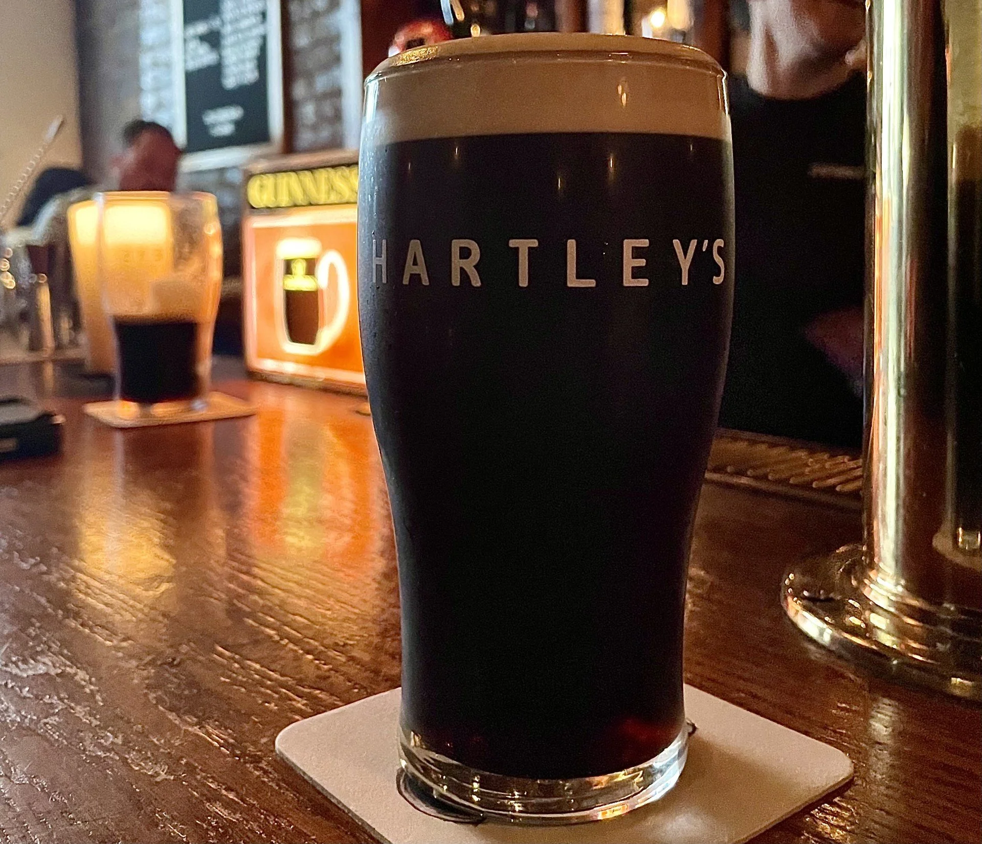 A pint of Guinness in a Hartley's branded pint glass on a bartop.