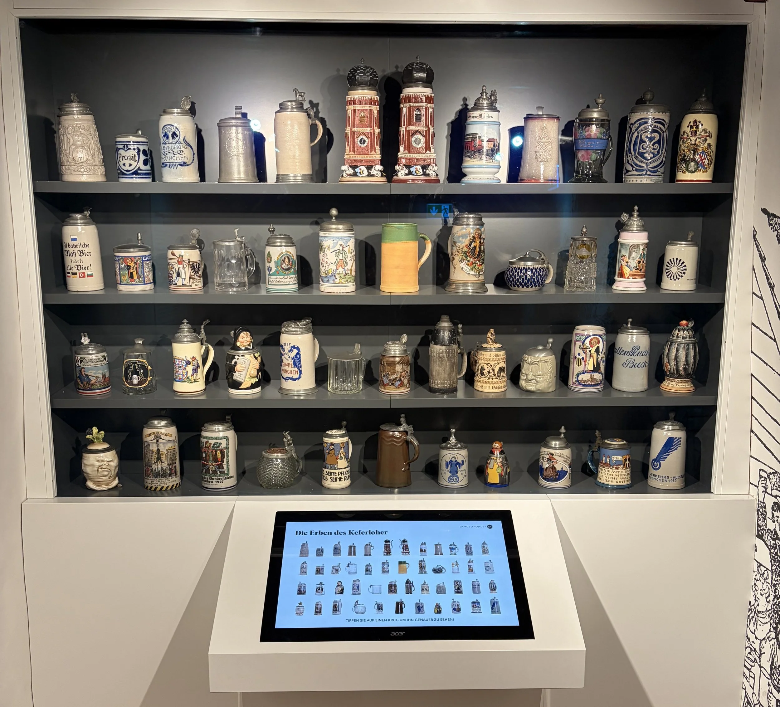 Interactive display at the  the Beer and Oktoberfest Museum with several shelves of drinkware and a screen in front of it that provides information on each.