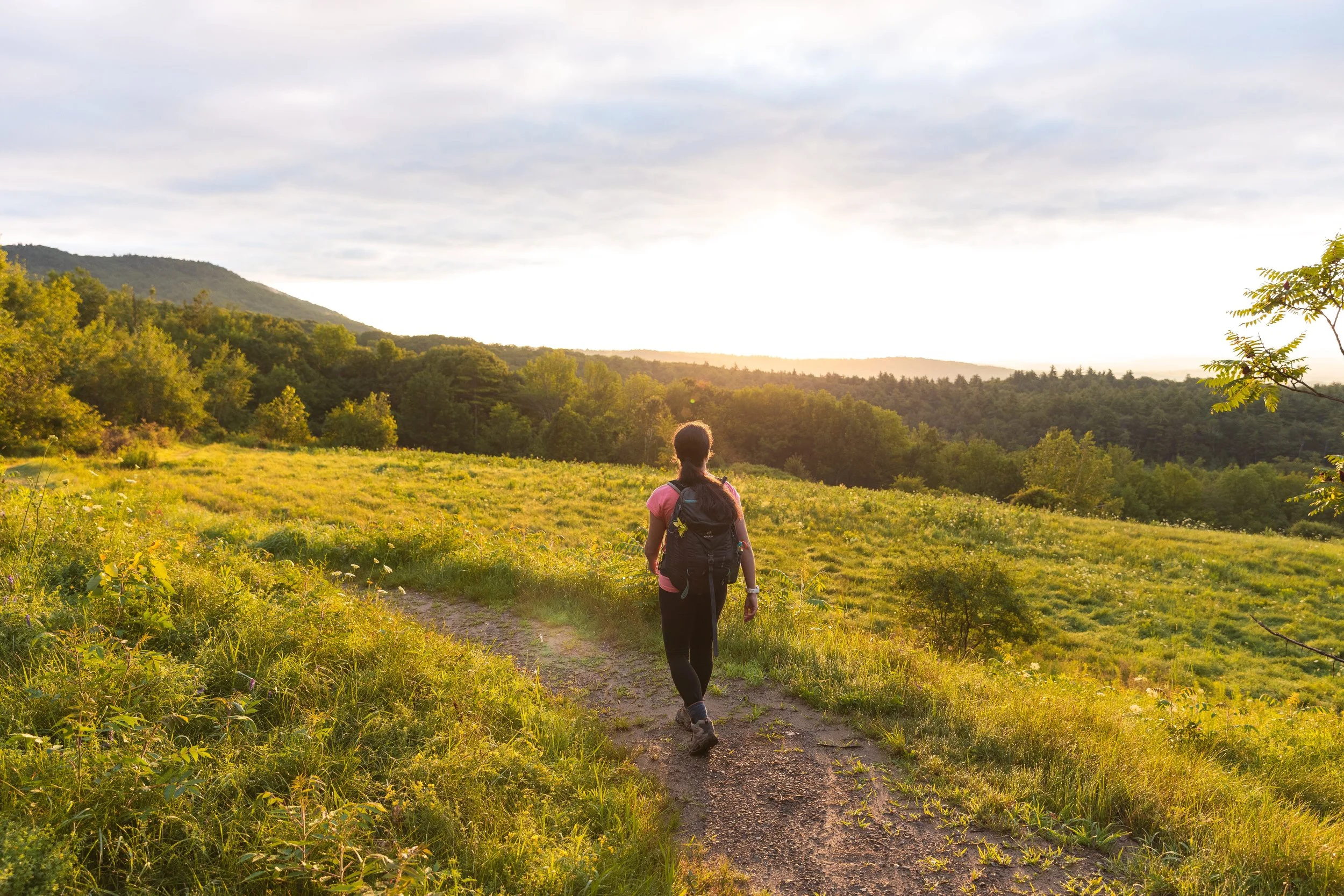 girl hiking on grassy trail overlooking sunrise