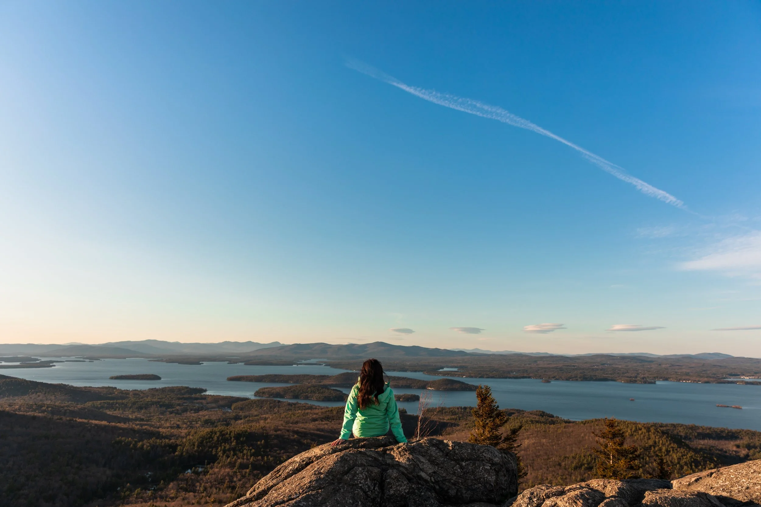 girl sitting on rock on mount major overlooking lake winnipesaukee