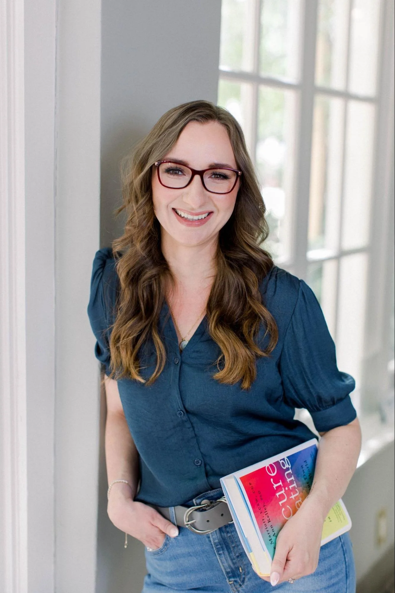 Young woman with long wavy hair smiling outdoors in front of a large cactus and sandy landscape.