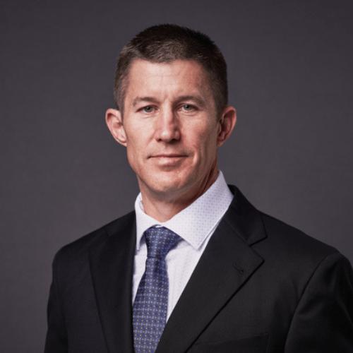 Professional man in a suit and tie with short brown hair posing against a dark gray background.